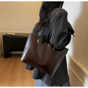 Detail of a dark brown glossy leather bucket tote bag with gold metal hardware and slim strap