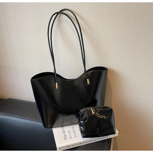 Detail of glossy black tote bag and matching pouch on a minimalist sofa background