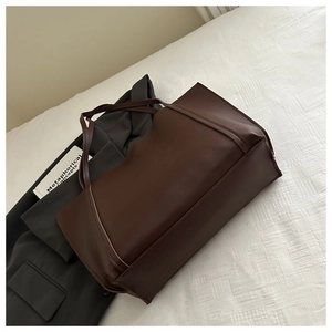 Detail of a large dark brown matte leather tote bag styled on a grey blazer and white bed