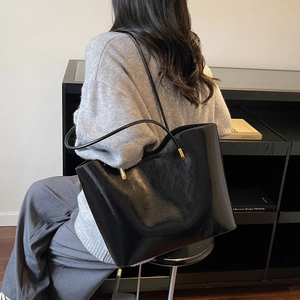 Minimalist black glossy leather tote bag with gold hardware shown on a model