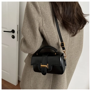 Detail of black glossy leather handbag with gold metal clasp and adjustable strap