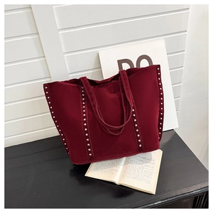 Détail du sac cabas en daim bordeaux avec rivets métalliques sur un fond minimaliste