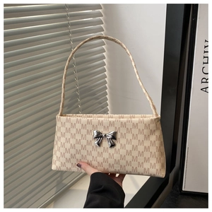 Detail of a chic cream underarm bag with M-letter print and silver metal bow decoration