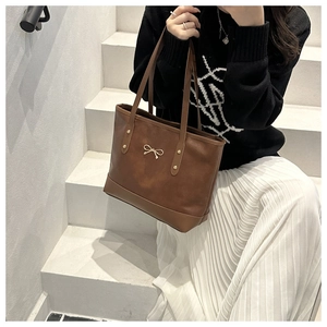 Deep brown leather tote bag with gold bow detail and metallic studs on white stairs