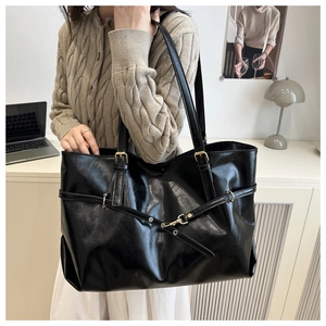 Detail of black faux leather tote bag with unique cross strap and gold buckle accent