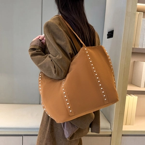 Sac cabas en daim marron avec rivets métalliques et longues anses porté à l'épaule
