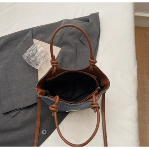 Dettaglio borsa a spalla in denim con manici annodati in pelle marrone e zip di chiusura