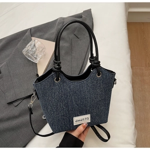 Dettaglio borsa denim con bordo ondulato ed etichetta in pelle su un blazer grigio scuro