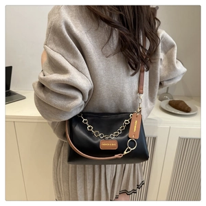 Detail of black crossbody pillow bag featuring golden floral chain and leather brand tag