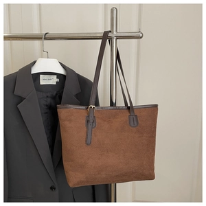 Detail of brown suede tote bag featuring dark leather trim and gold metal adjustment buckle