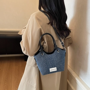 Borsa a secchiello in denim retrò con manici in pelle e tracolla indossata da modella