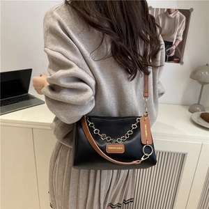 Chic black leather crossbody bag with chain and brown strap on a minimalist desk