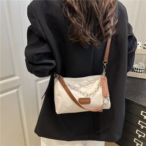 White nylon shoulder bag with brown strap and golden floral chain worn by a model