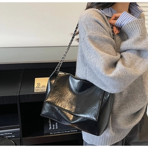 Detail view of black wrinkled patent leather shoulder bag with a metal chain strap