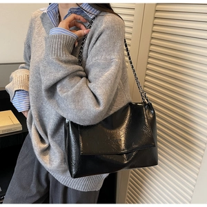 Detail of black pleated leather shoulder bag with silver chain strap on model