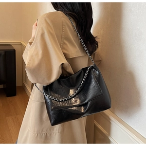 Detail der schwarzen glänzenden Schultertasche mit Silberkette zum khakifarbenen Trenchcoat