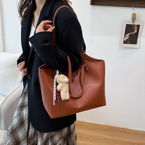 Brown leather tote bag with long handles and a cute plush bear pendant accessory