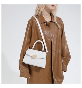 Detail of white quilted leather bag with gold metal buckle on a brown coat background