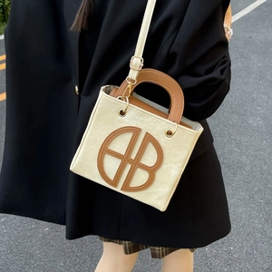 Elegant beige tote bag with brown artistic lettering and dual handles in urban street setting