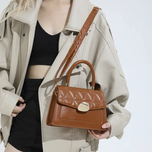 Brown quilted leather shoulder bag with gold buckle worn by model in beige jacket