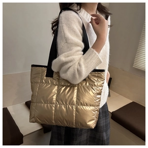 Detailed shot of gold quilted puffer tote bag on shoulder with black strap detail