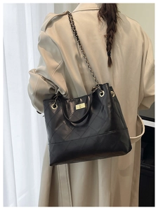 Dettaglio della borsa tote trapuntata nera con catena d'oro indossata su un trench beige