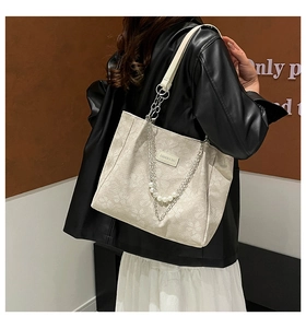 Detail of cream tote bag with floral embossing, metal chains and pearl accents