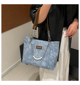 Detail of light blue floral tote bag with brown leather straps and pearl chain accessory