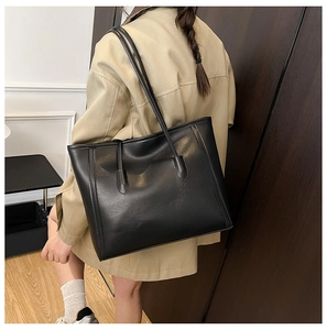 Vista laterale di una grande borsa tote in pelle nera indossata da una modella in abiti autunnali