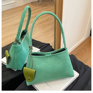 Détail du sac à main vert givré avec pendentif en cuir posé sur une surface de miroir