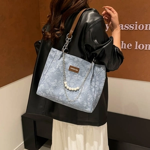 Blue floral tote bag with brown leather strap and pearl chain detail worn by a model