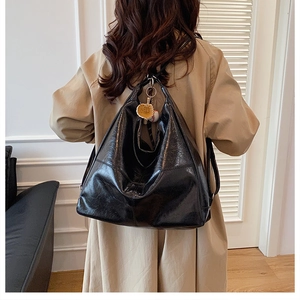 Rear view of black glossy tote bag with baseball charms worn over a beige trench coat