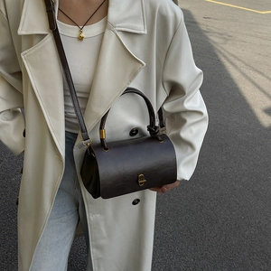 Retro brown cylinder handbag with gold hardware shown in an outdoor lifestyle setting