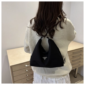 Detail of black nylon backpack featuring a silver triangular plaque and metal chain