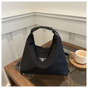 Detail of black nylon Hobo bag with metal chain strap and logo plaque on a wooden table