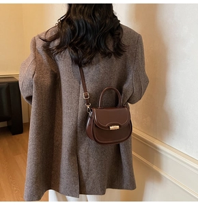 Detail of dark brown saddle bag with golden clasp worn over a gray wool blazer
