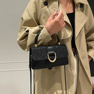 Sac à main chic noir avec empiècement pailleté et boucle dorée porté sur un trench-coat