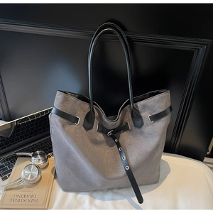 Detail of grey suede tote bag with black leather straps next to a laptop and books