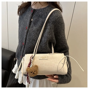 Detail view of cream shoulder bag featuring side lace-up design and cute teddy bear charm