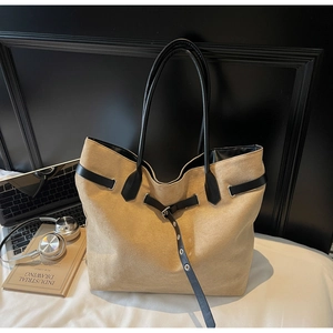 Detailed view of khaki suede tote bag with black leather straps in a home office setting