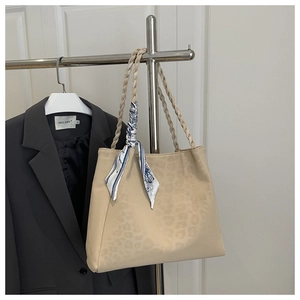 Detail of leopard print tote bag featuring woven handles and decorative blue silk scarf