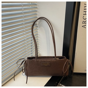 Detail of a brown suede tote bag featuring chic side ribbon bows and a logo plaque