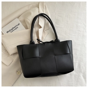 Détail du sac fourre-tout tissé noir sur un fond en tissu texturé de couleur crème