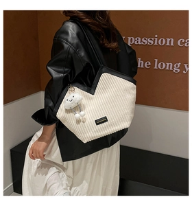 Close-up of white corduroy tote bag with black leather trim and plush cloud charm