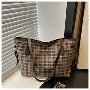 Detail of checkered tote bag with brown leather handles and central patch ornament