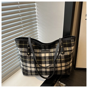Detail of tweed checkered tote bag showing black leather strap and golden rivet accents