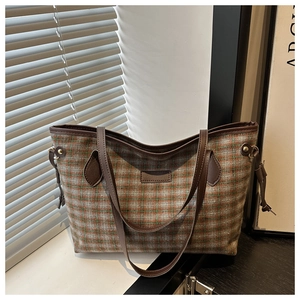 Detailed view of checkered tote bag with brown leather straps by a sunlit window