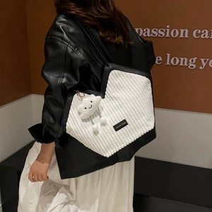 White corduroy tote bag with black trim and plush cloud charm shown on shoulder