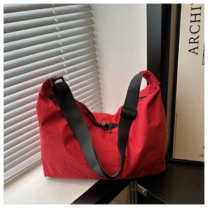 Detailed shot of red nylon pillow bag featuring a wide black strap and double silver zippers