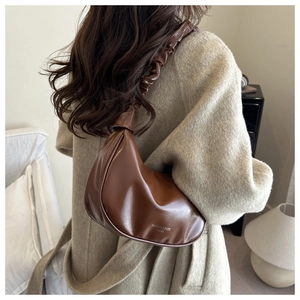 Détail d'un sac baguette marron à anse froncée porté avec un manteau beige élégant